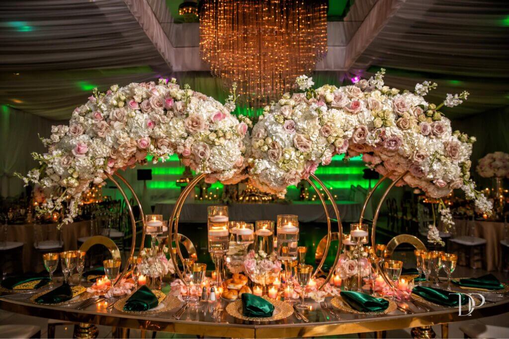 Luxurious wedding table with large cascading floral arrangements, gold accents, floating candles, and elegant place settings at Eden Regal Ballroom.